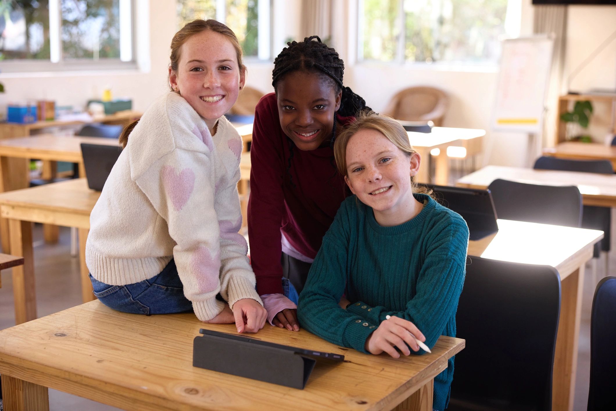 Three schoolgirls smiling together in a bright classroom while learning collaboratively